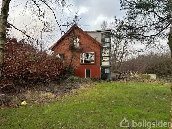 Et rødt hus står stille i en åben have omgivet af træer og buske. Huset har store vinduer og et glaspanel på siden. Uden tekst.