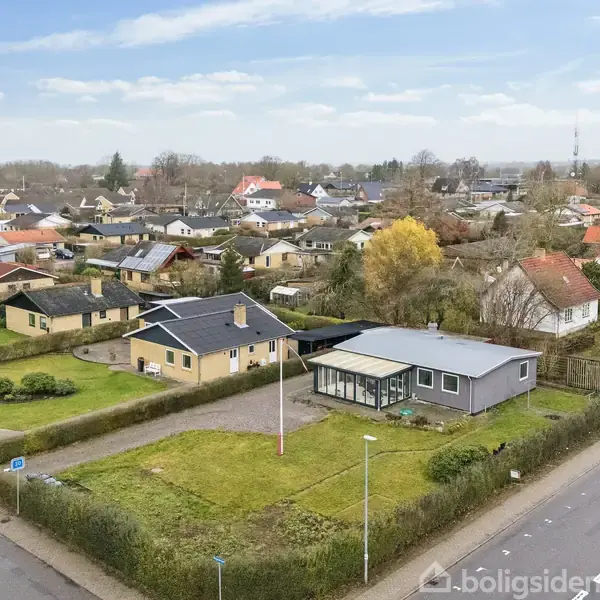 En moderne villa med fladt tag står i en velholdt have omgivet af hække. Huset ligger i et roligt, parcelhuskvarter med flere ensartede huse og velplejede haver omkring sig.