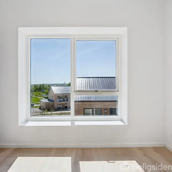 Vindue i hvid væg viser udsigt til et moderne hus med metaltag og grønt område udenfor, under en klar blå himmel. Gulvet er lyst trægulv.