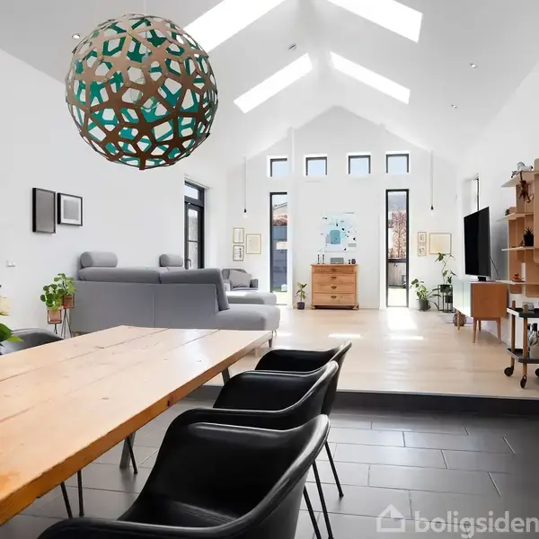 En moderne stue med træbord og sorte stole, domineret af en geometrisk lampe over bordet. Rummet har store vinduer, hvide vægge og grå sofa i et lyst miljø.