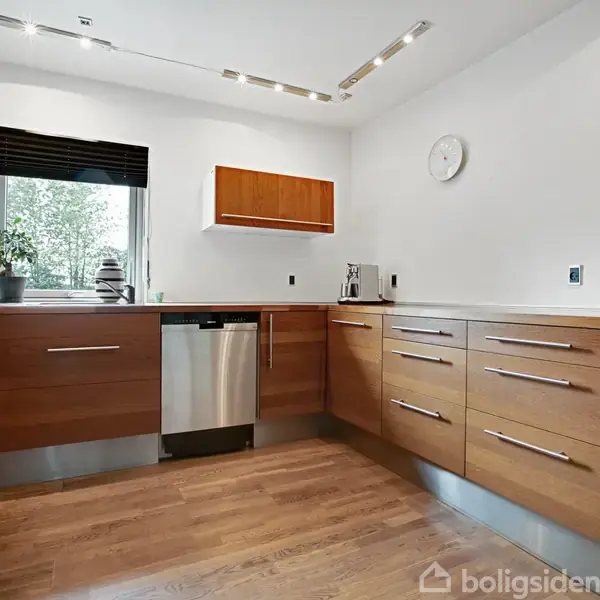 Et moderne køkken med træskabe og skuffer. En opvaskemaskine er monteret ved siden af en håndvask. Et vindue med rullegardin slipper lys ind. På væggen hænger en plakat med teksten "We can do everything". En hvid vægur pryder væggen.