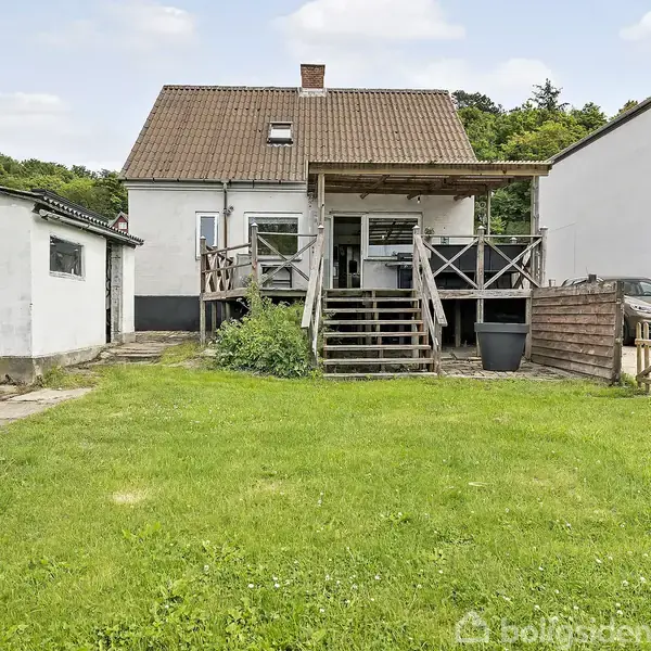 Dør i entré står lukket ved siden af en hvid trappe, der fører opad. Stanley-værktøjskasse er placeret på gulvet, mens en knagerække hænger på væggen.