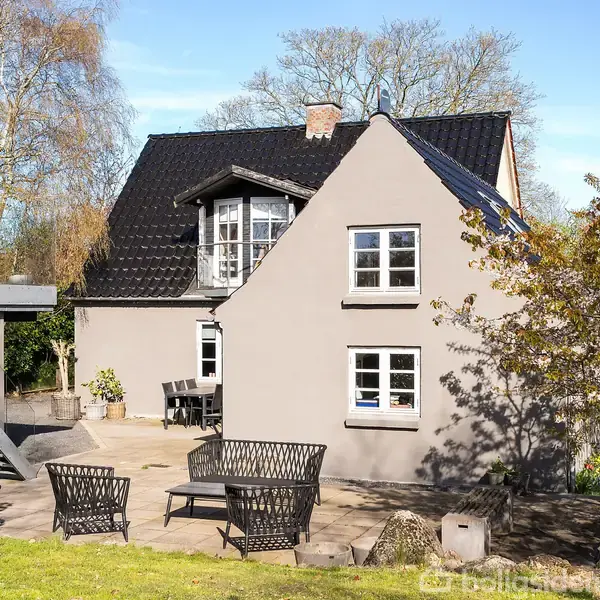 Sort havemøbelsæt står på en flisebelagt terrasse. Det er omgivet af blomstrende træer og græsplæne under en klar himmel.