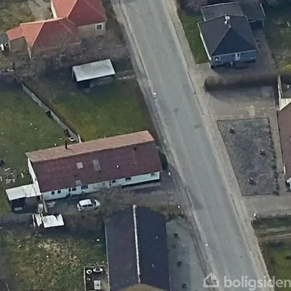 Tofamiliehus med rødt tag og hvid facade står stille. Beliggende i en have ved siden af en vej med en parkeret bil foran.
