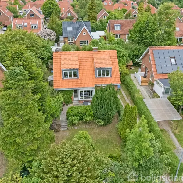 Et rødt tegltagshus med to etager er omgivet af grønne træer og hække. Huset har en lille have foran med en sti. Omgivet af lignende huse i et boligkvarter.