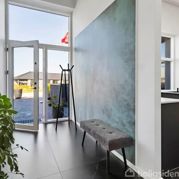 En indgang med en åben glasdør leder til en have. En stumtjener står ved siden af en bænk. Planter pynter det moderne rum op.