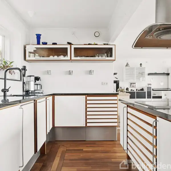 Et hus med fladt tag og garageporte står i en bakkedækket have ved stranden, med udsigt over havet og en stor græsplæne.