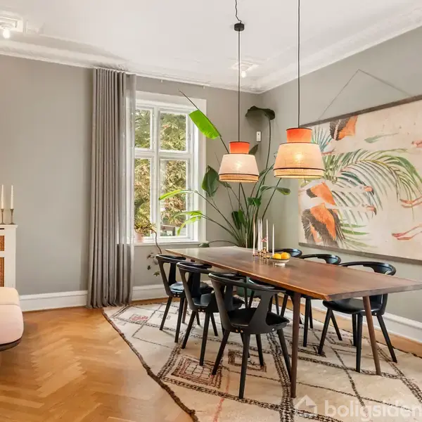 Spisebord med seks stole står i en elegant spisestue med træparketgulv. Store vinduer lader lys ind, og væggene er dekoreret med kunst og planter. Ingen tekst fundet.