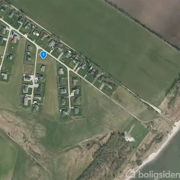 Bebyggelse markeret med en blå nål, omgivet af grønne marker og skov. Veje forbinder huse, mens en kystlinje løber langs højre side.