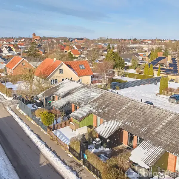 Rækkehuse dækket af et tyndt lag sne står side om side i en boligkvarter. Omgivelserne inkluderer sneklædte haveområder og en tætpakket vej.