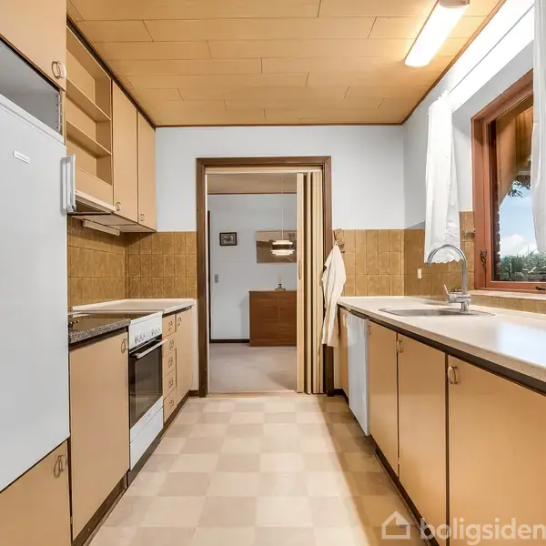 Køkken med beige skabe og hvide bordflader, aktiviteter inkluderer madlavning og oprydning, konteksten viser et vindue med udsigt og en åbning til en tilstødende stue.