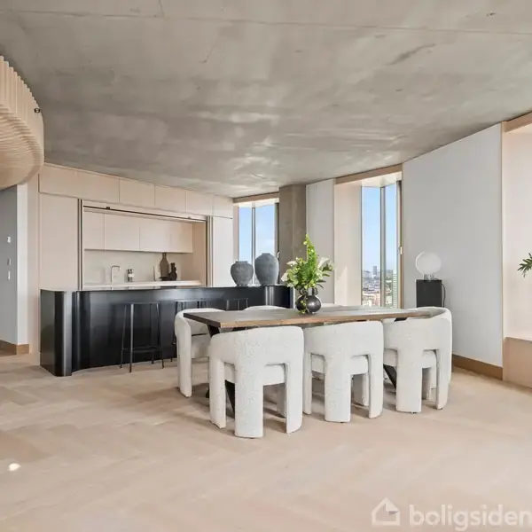 En elegant spisestue med et moderne bord og seks polstrede stole. Store vinduer slipper lys ind. I baggrunden er der et sort køkken, og planter tilføjer grønne detaljer.