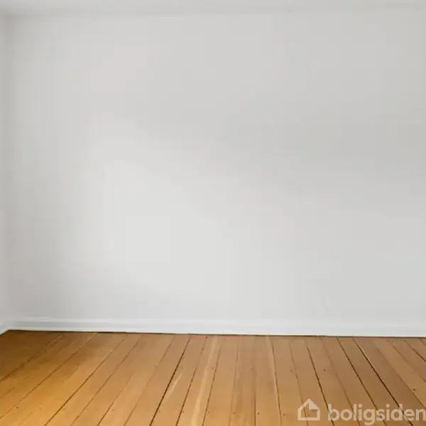 Et tomt værelse har hvide vægge og et trægulv, set fra et hjørne. Et vindue til venstre lader lys komme ind i rummet.