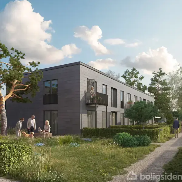 Moderne lejlighedskompleks med grå facader og altaner, hvor havemøbler står klar. I forgrunden ses en velplejet græsplæne og gangsti under en næsten skyfri, blå himmel.
