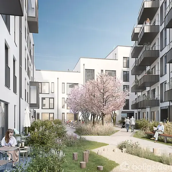 Et moderne lejlighedskompleks omgiver en gårdhave, hvor mennesker sidder og nyder udendørsområdet. En sti snor sig gennem græs og en blomstrende træ, der tilføjer farve og liv.