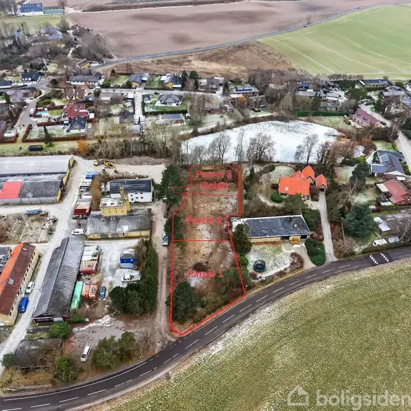 Luftfoto viser tre ledige byggegrunde markeret som "Parcel 1," "Parcel 2," og "Parcel 3" med røde linjer i et boligområde. Omgivet af huse og grønne marker.