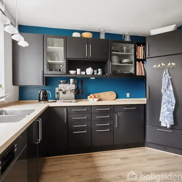 Køkken med sorte skabe og skuffer arrangeret i en L-form. Opvaskemaskine, kaffemaskine og kogebøger er synlige. En stor vindueskarm med planter giver naturligt lys.