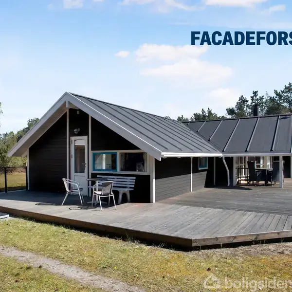 Et sort træhus med skråt tag står på en stor træterrasse. En bæk og stole er placeret udenfor. Skov og klar blå himmel omkranser huset. Tekst: "FACADEFORSLAG".