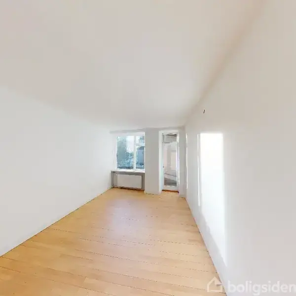 Et tomt rum med lyse træplanker på gulvet. Et vindue for enden tillader dagslys at strømme ind. Hvide vægge skaber et lyst og rummeligt udseende.