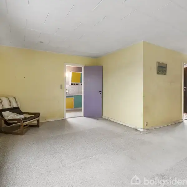 Stue med en enkelt stol placeret ved et vindue, hvor der står en plante. Rummet har gul vægge og tæppebelagt gulv. Døre fører til andre rum.