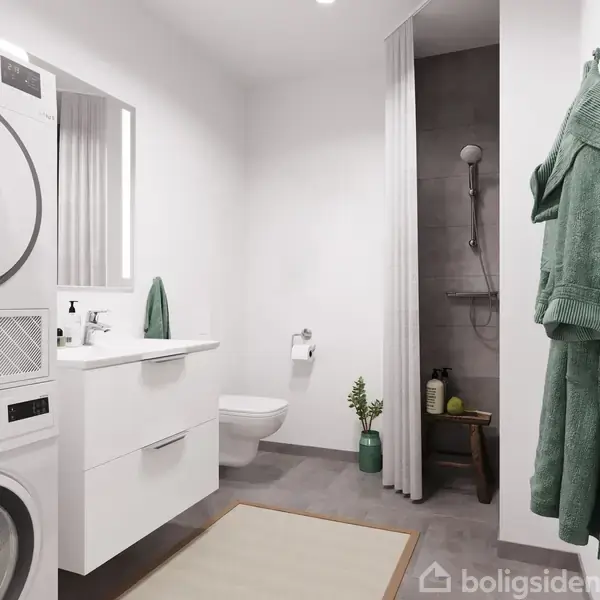 En moderne vaskemaskine står i et lyst badeværelse, ved siden af et indbygget toilet og en vask med spejl. Der er en bruser i et aflukke med gardin.