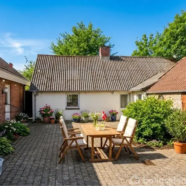 En gårdhave med et træbord og seks stole. Bordet er fyldt med drikkeglas. Omkring står potteplanter. Hvide og røde bygninger omkranser gårdspladsen, og der er blå himmel og træer i baggrunden.