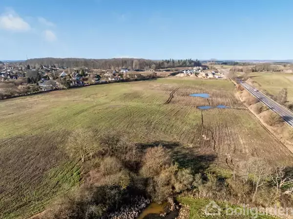 Sø omgivet af boliger; rolige kvarterer spredt langs bredden. Området strækker sig mod en skov i horisonten under en klar blå himmel.