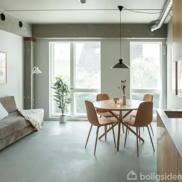 Stue med spisebord og fire stole står i midten af rummet. En sofa og gulvlampe er til venstre. Store vinduer giver udsigt og lys. En plante står i hjørnet.