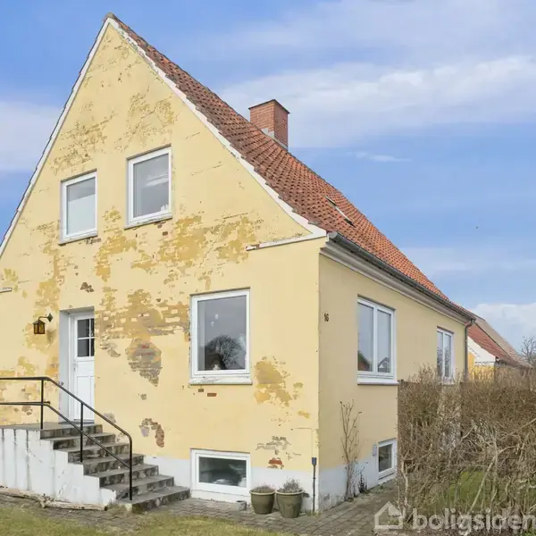 Et gult murstenshus med skråt tag står i en have med en trappe foran indgangen. Huset har hvide vinduer og en hæk omkranser grunden under en blå himmel.