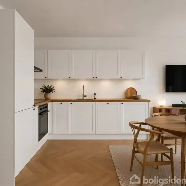 Et moderne køkken med hvide skabe står ved siden af en rund spisebord med stole. En plante og dekorative genstande er på bordet, mens et vægmonteret TV hænger i stuen.