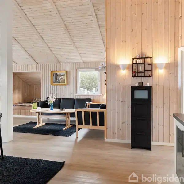 Huse med røde tage står stille nær kysten med udsigt over havet. Omgivet af grønne marker og andre boliger, skaber de en fredfyldt sommerhus-atmosfære.