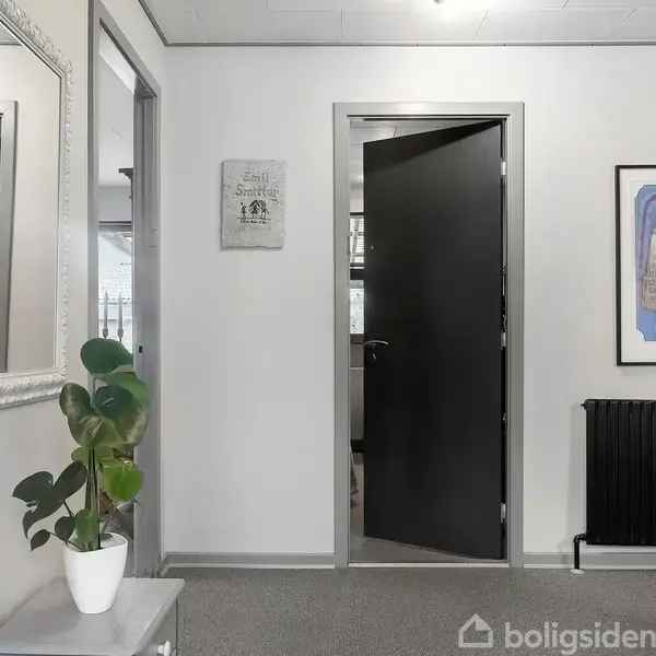 Dør åbner indad i en lys gang med gråt gulvtæppe. Spejl og plante til venstre. Tekst på skilt: "Sweet Smell of Success". Billedramme og radiator til højre.