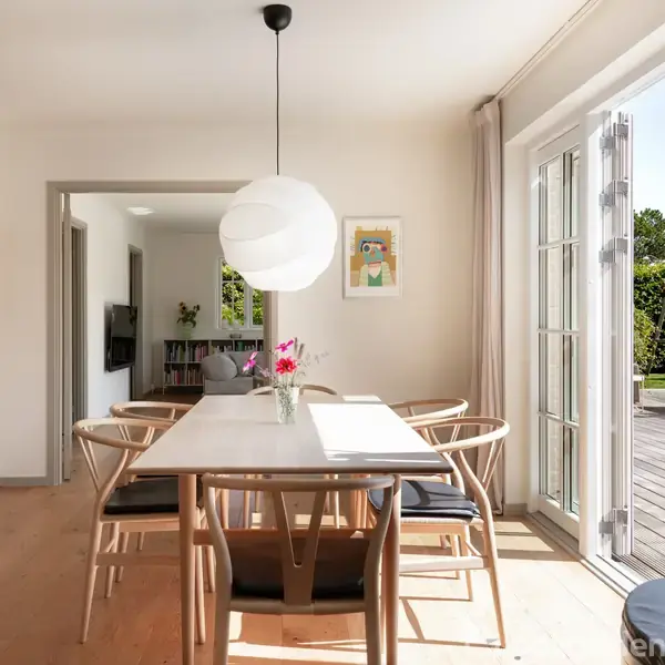 Et spisebord med seks stole står i et lyst rum. Bordet har en vase med blomster og en rund lampe hænger over det. Terrassedøre åbner ud til en træterrasse.