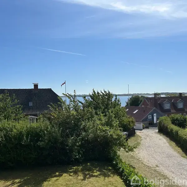 Brusekabine med bruser hænger på væggen. Rummet har flisevægge. Ved siden af er der en trappe op til overetagen i et lyst gangareal med flisegulv.