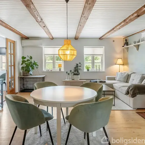 En stue med et rundt hvidt spisebord og fire grønne stole. Der hænger en gul lampe over bordet. I baggrunden står en sofa ved siden af et vindue, omgivet af planter og hylder.