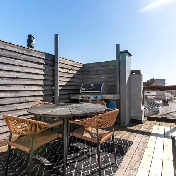 To sofagruppe står på et tæppe i en lys stue med parketgulv. Et lille rundt bord står imellem dem, mens planter og store vinduer fylder rummet med lys.