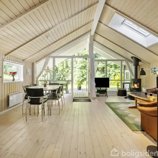 Stue med træbeklædte vægge og loft, brændeovn, brunt lædermøbel og spisebord. Store glasdøre leder ud til terrasse med udsigt til grøn have. Klar og lys atmosfære.