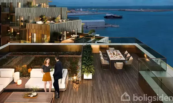 Et par står og taler på en moderne tagterrasse med sofaer og et spisebord. Omkring dem er beboelsesbygninger med udsigt over vandet, hvor et skib passerer forbi.