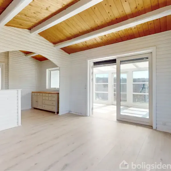 Rummeligt, lyst lokale med træloft og lyse gulve, der fører ud til en solrig terrasse gennem store glasskydedøre. Et hvidt vægpanel og en skænk er synlige.