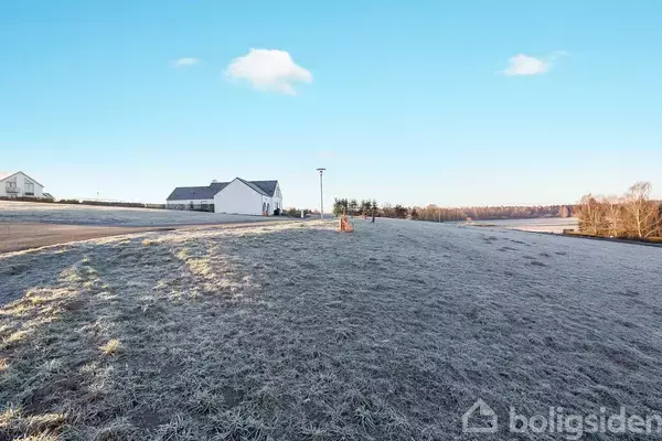 Hus står stille på en frostbeklædt mark med blå himmel, nogle træer i baggrunden og en vej foran.