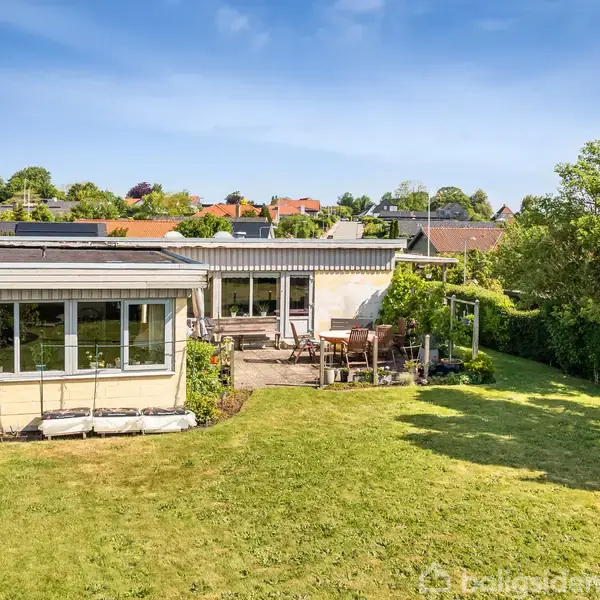 En enkelt-etagers lysegul bygning med store vinduer; omgivet af en grøn have med græsplæne og træer; i en stille forstad; under en klar blå himmel.