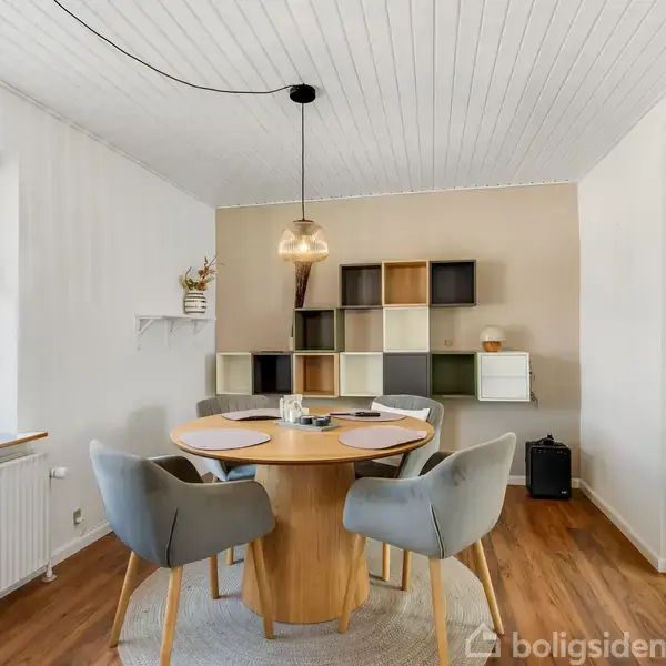 Et rødt murstenshus med en tilbygning af træ har to liggestole foran. Omkring er en velplejet græsplæne med en sandkasse og buske. Himlen er blå med få skyer.