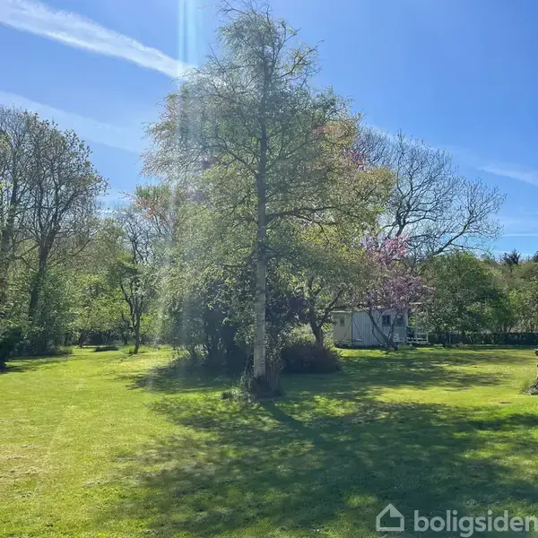 En entré med en hvid bænk og spejl, beliggende ved siden af en trætrappe. En dør fører ud til venstre, og der hænger frakker på knager. Gulvet er flisebelagt.