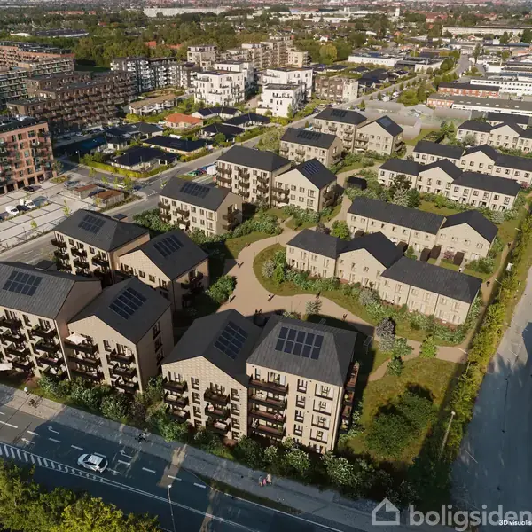 Boligkompleks set fra oven, bygninger med solpaneler. Bygningerne er grupperet omkring grønne områder og stier. Udsyn over byområde med flere boligblokke i baggrunden.