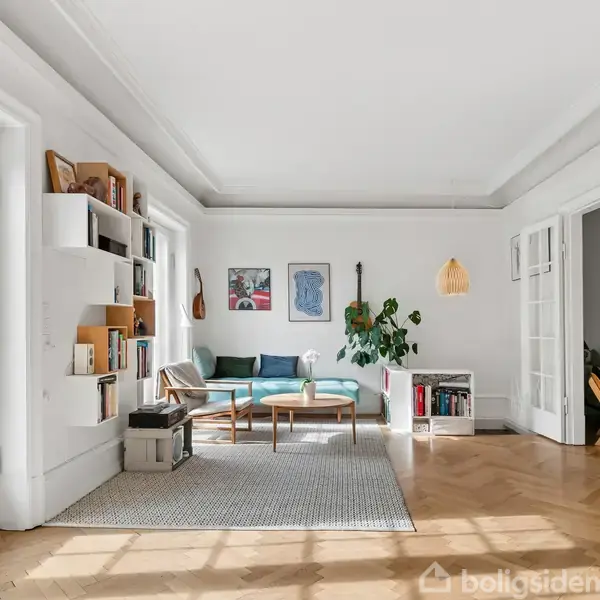 Stue med sofa i hjørnet, reol med bøger og dekorationer på væggen. Store vinduer og døre indrammer rummet, som er lyst med parketgulv. En plante og kunstværker tilføjer farve.