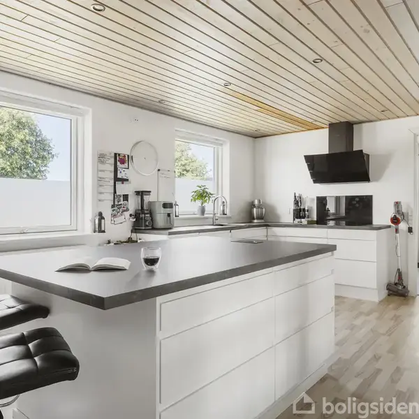 Køkken med hvid ø, to sorte barstole og moderne apparater. Omgivet af lyse trævægge og vinduer, der giver naturligt lys. En bog og et vinglas står på øen.