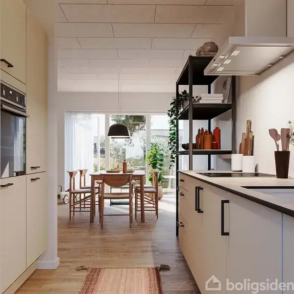 Et moderne køkken med hvide skabe strækker sig mod en spisestue. Køkkenet har planter og kokkelredskaber på bordet. I baggrunden står et rundt spisebord ved et stort vindue.