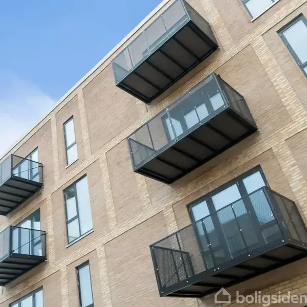 En moderne bygning med tre niveauer af sorte metalbalkoner, der strækker sig fra murstensfacaden. Mange vinduer på facaden. Skyfri blå himmel i baggrunden.