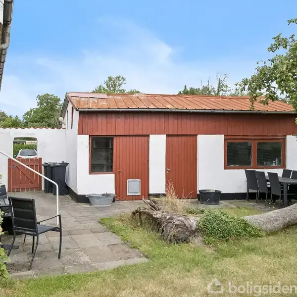 Et rødt murstenshus med et brunt tegltag; en sølvfarvet bil holder parkeret foran. Haven omgiver huset, og træer er synlige i baggrunden.
