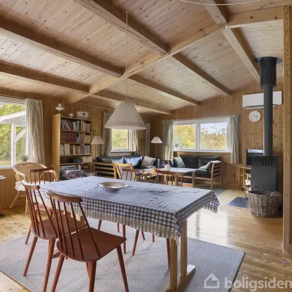 Træbeklædt stue med spisebord dækket med ternet dug. Rummet indeholder brændeovn, sofaer ved vinduer og bogreol. Lysindfald fra store vinduer. Atmosfæren er hyggelig og naturlig.